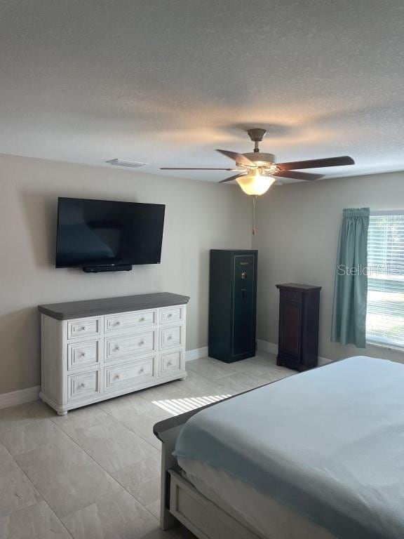 bedroom featuring ceiling fan, light tile patterned floors, and a textured ceiling