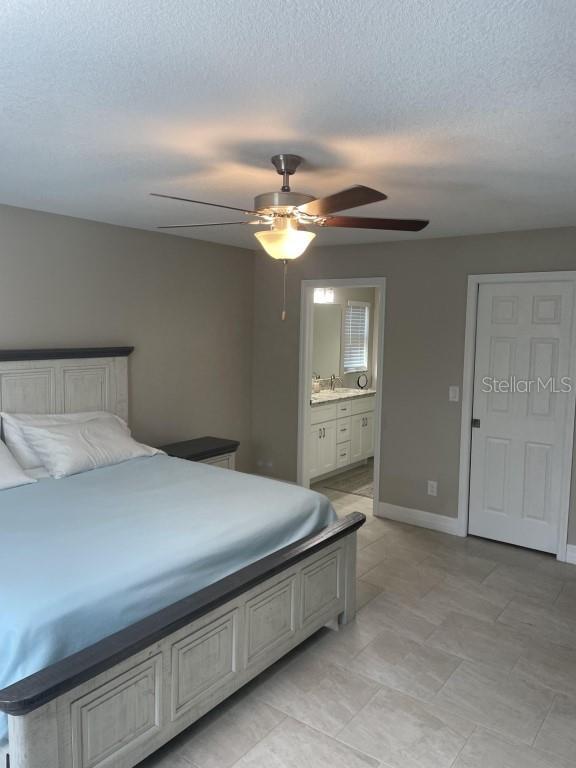 bedroom with a textured ceiling, ensuite bathroom, and ceiling fan