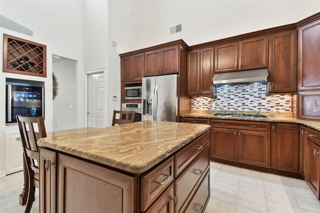 kitchen featuring wine cooler, extractor fan, light stone counters, appliances with stainless steel finishes, and a kitchen island