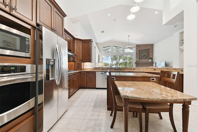 kitchen with lofted ceiling, light stone counters, hanging light fixtures, appliances with stainless steel finishes, and kitchen peninsula