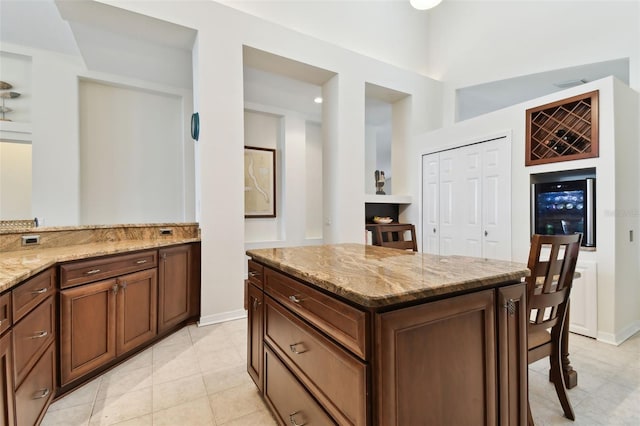 kitchen featuring wine cooler, light stone countertops, a kitchen island, and light tile patterned floors