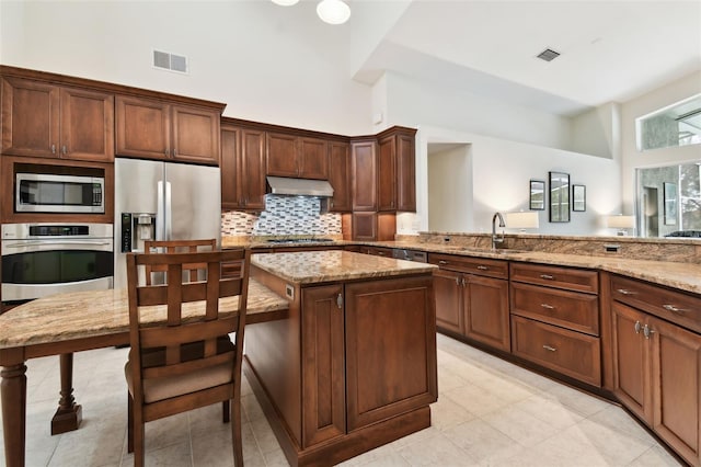 kitchen featuring sink, light stone counters, appliances with stainless steel finishes, a kitchen island, and range hood