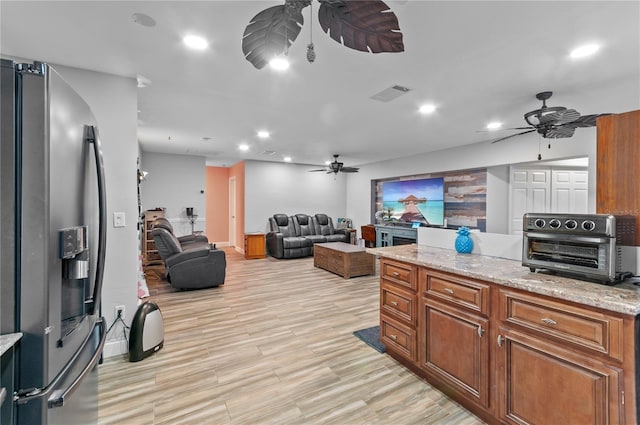 kitchen featuring light stone counters, stainless steel fridge, light hardwood / wood-style floors, and ceiling fan