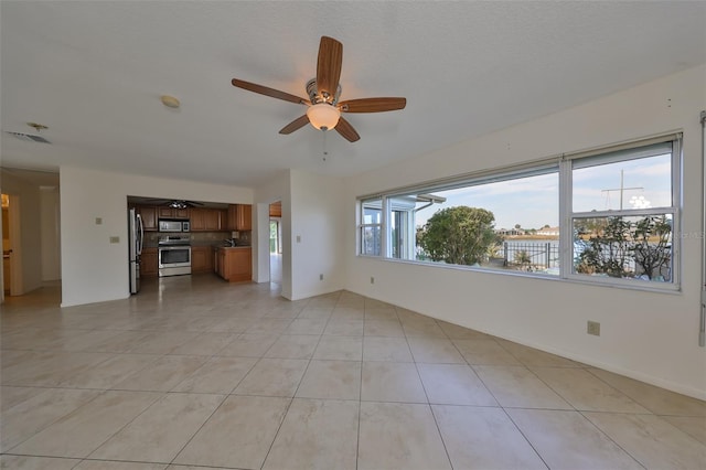 unfurnished living room featuring ceiling fan, a healthy amount of sunlight, light tile patterned floors, and a textured ceiling