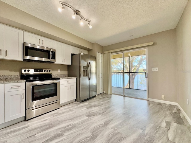 kitchen featuring light stone counters, white cabinetry, a textured ceiling, and appliances with stainless steel finishes