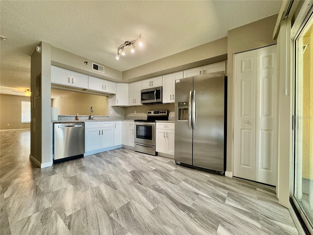 kitchen with appliances with stainless steel finishes, a textured ceiling, white cabinetry, and sink