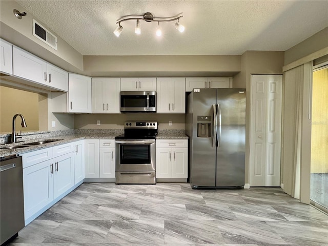 kitchen featuring sink, a textured ceiling, appliances with stainless steel finishes, light stone counters, and white cabinetry