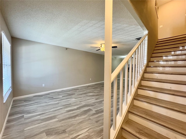 staircase with wood-type flooring, a textured ceiling, and ceiling fan