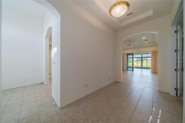 tiled spare room with ceiling fan and a tray ceiling