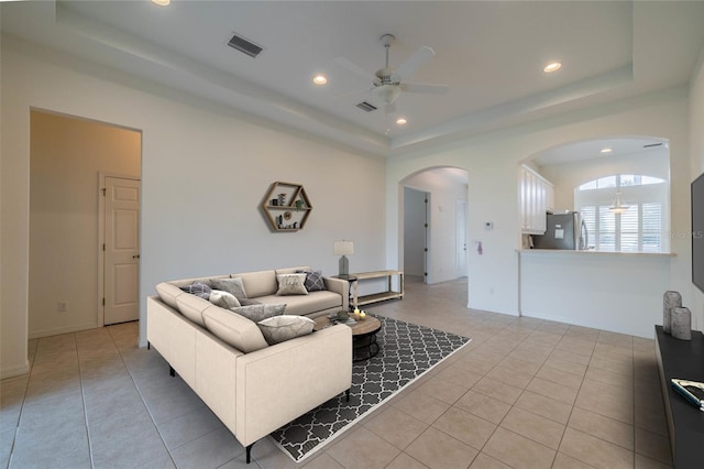 living room featuring a raised ceiling, ceiling fan, and light tile patterned flooring