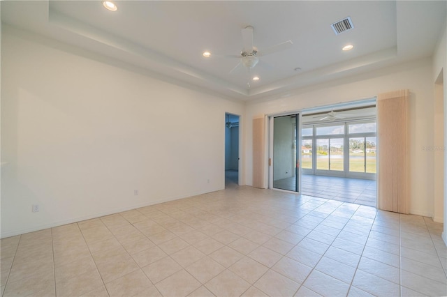 empty room with light tile patterned floors, ceiling fan, and a tray ceiling