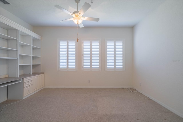 unfurnished office with light carpet, built in desk, and ceiling fan