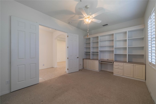 unfurnished bedroom featuring multiple windows, built in desk, light colored carpet, and ceiling fan