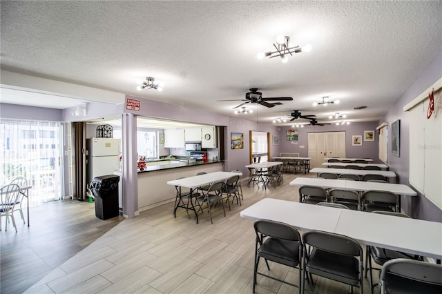 dining room featuring ceiling fan with notable chandelier, a healthy amount of sunlight, light wood-type flooring, and a textured ceiling