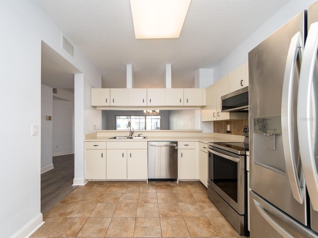 kitchen featuring sink, stainless steel appliances, a textured ceiling, cream cabinetry, and light tile patterned floors