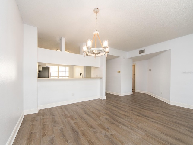 unfurnished living room featuring a chandelier, wood-type flooring, and a textured ceiling