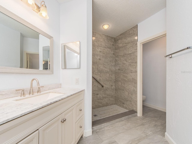 bathroom with vanity, a textured ceiling, tiled shower, and toilet