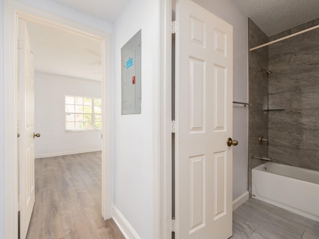 bathroom with a textured ceiling, electric panel, hardwood / wood-style floors, and tiled shower / bath combo