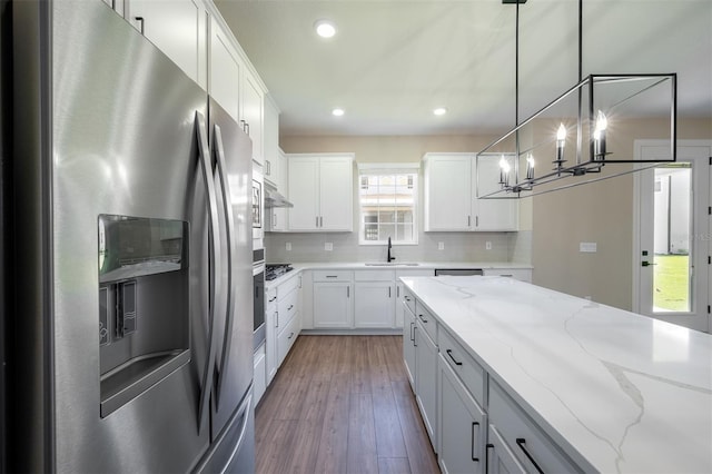 kitchen featuring stainless steel fridge, light stone counters, hardwood / wood-style floors, white cabinetry, and hanging light fixtures