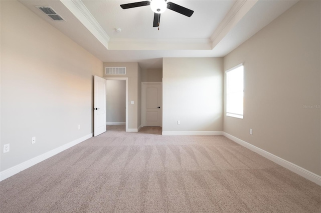 empty room with ceiling fan, light colored carpet, ornamental molding, and a tray ceiling