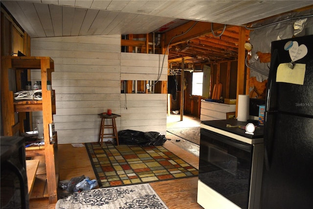 kitchen with tile countertops, vaulted ceiling, wooden walls, black refrigerator, and hardwood / wood-style flooring