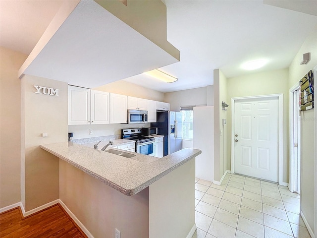 kitchen with kitchen peninsula, appliances with stainless steel finishes, sink, light tile patterned floors, and white cabinetry