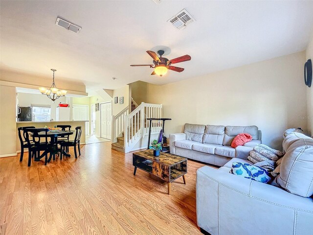 living room featuring ceiling fan with notable chandelier and light wood-type flooring