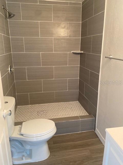 bathroom featuring toilet, hardwood / wood-style floors, vanity, and tiled shower