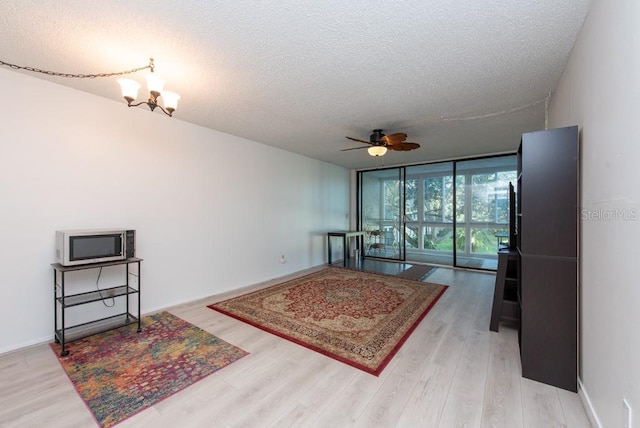 living room with wood-type flooring, ceiling fan with notable chandelier, a textured ceiling, and a wall of windows