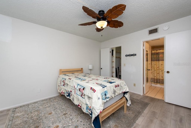 bedroom featuring hardwood / wood-style floors, ensuite bathroom, ceiling fan, and a textured ceiling