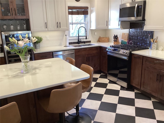 kitchen with white cabinets, dark brown cabinetry, stainless steel appliances, and sink