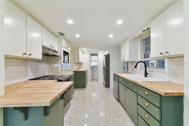 kitchen with appliances with stainless steel finishes, butcher block counters, white cabinetry, and under cabinet range hood