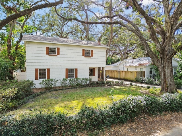 view of front facade with brick siding, fence, and a front lawn