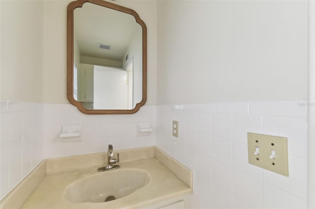 bathroom with a wainscoted wall, tile walls, visible vents, and a sink