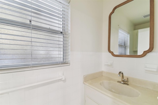 bathroom with a wainscoted wall, plenty of natural light, tile walls, and vanity