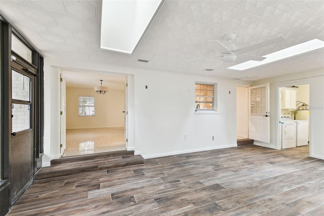 unfurnished room featuring a skylight, washing machine and clothes dryer, ceiling fan, wood finished floors, and baseboards