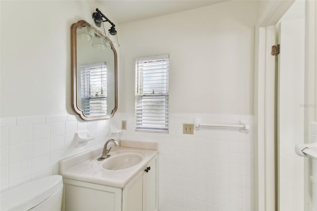 half bath with tile walls, wainscoting, and vanity