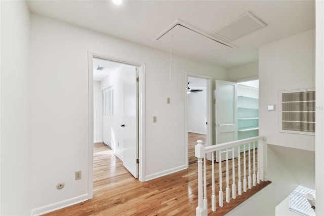 hallway featuring light wood-style floors, attic access, visible vents, and an upstairs landing