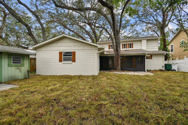 rear view of property with a sunroom, brick siding, a yard, and fence