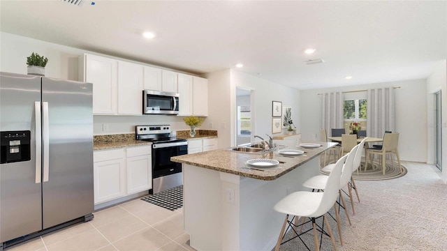 kitchen with sink, stainless steel appliances, an island with sink, light colored carpet, and white cabinets