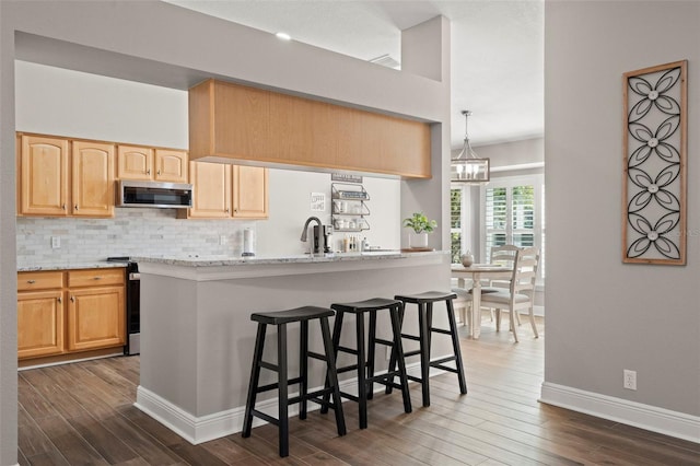 kitchen with light brown cabinetry, decorative light fixtures, backsplash, light stone counters, and dark hardwood / wood-style floors