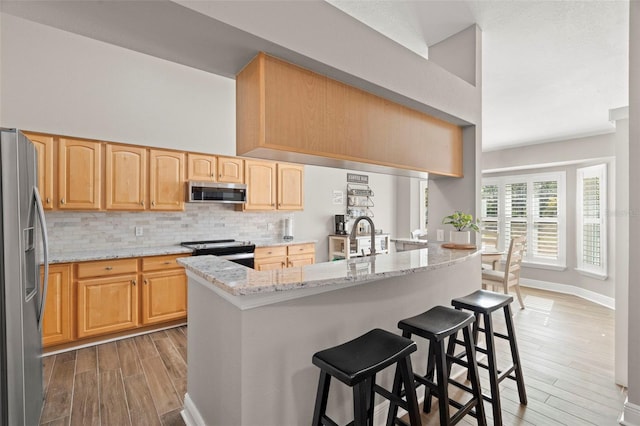 kitchen featuring appliances with stainless steel finishes, decorative backsplash, a kitchen breakfast bar, kitchen peninsula, and light stone counters