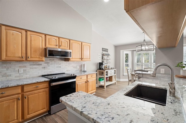 kitchen with decorative light fixtures, light stone counters, sink, and stainless steel appliances