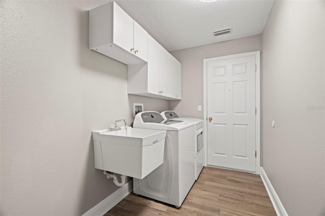 laundry room featuring sink, washing machine and clothes dryer, a textured ceiling, and cabinets