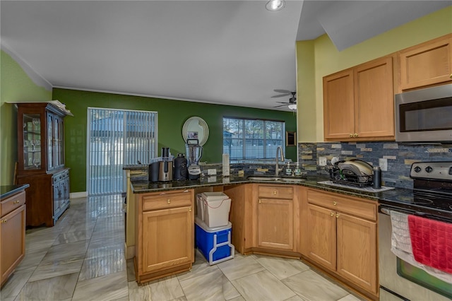 kitchen featuring kitchen peninsula, decorative backsplash, dark stone counters, stainless steel appliances, and sink