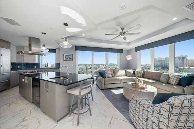 kitchen featuring sink, hanging light fixtures, an island with sink, tasteful backsplash, and island exhaust hood