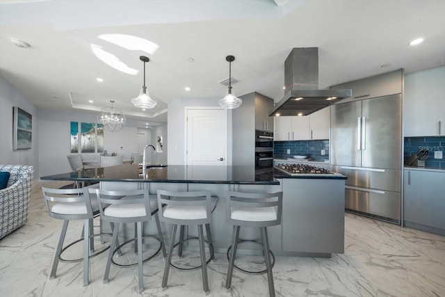 kitchen featuring backsplash, island exhaust hood, pendant lighting, a center island with sink, and appliances with stainless steel finishes