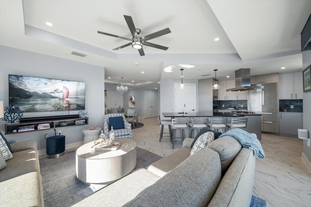 living room with a raised ceiling and ceiling fan with notable chandelier