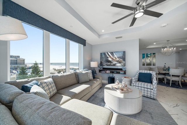 living room with a tray ceiling and ceiling fan with notable chandelier