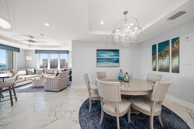 dining area with ceiling fan with notable chandelier and a tray ceiling